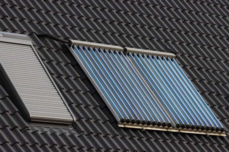Technicien en tenue professionnelle effectuant la mise en service d'une pompe à chaleur air-air installée, réglant le système de régulation et de contrôle sur l'unité intérieure murale, écran de commande visible, avec unité extérieure en arrière-plan montée sur support de façade.