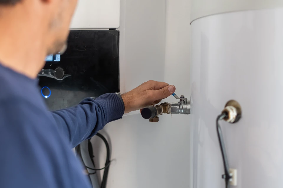Technicien en tenue professionnelle effectuant la mise en service d'une unité extérieure de climatisation ou pompe à chaleur, manipulant les raccords frigorifiques et utilisant un manifold de charge avec flexibles tricolores pour les vérifications de pression et d'étanchéité du circuit frigorifique.